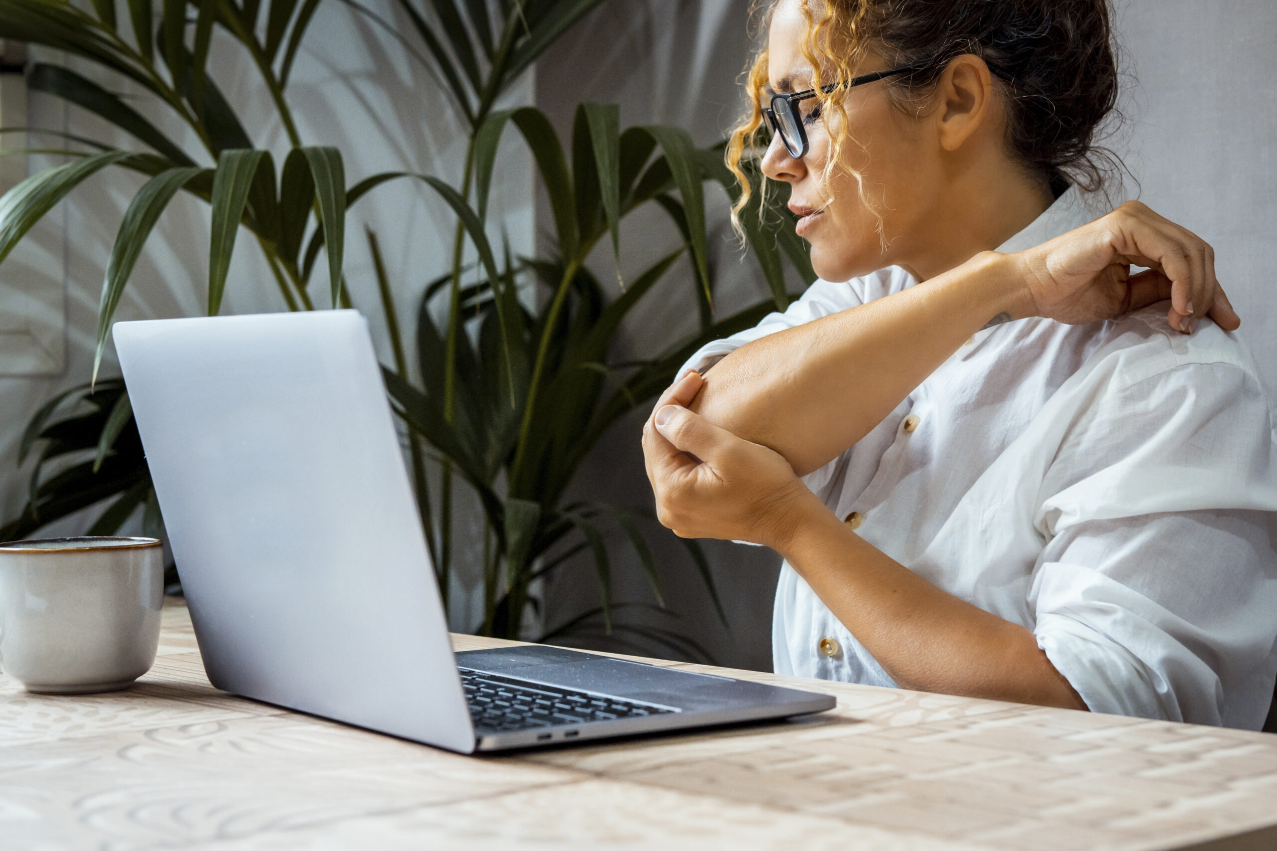 Ellenbogenschmerzen bei einer jungen Frau am Schreibtisch vor dem Laptop - Tennisarm durch Überlastung - Akupunktur kann helfen